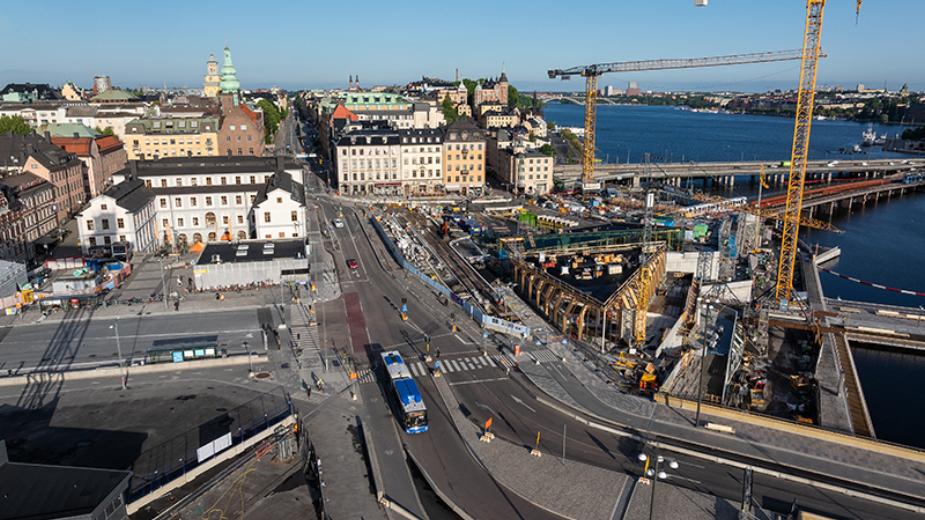Översikt över Slussen i Stockholm under byggnation, med kranar, broar och Gamla stan i bakgrunden.