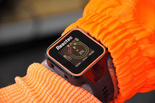 En närbild på en vibrationsklocka på en arm som bärs av någon i orange skyddskläder.