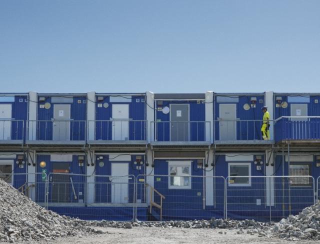 Tvåvånings etablering på en byggarbetsplats med en person i gul varselklädsel på övre gången.